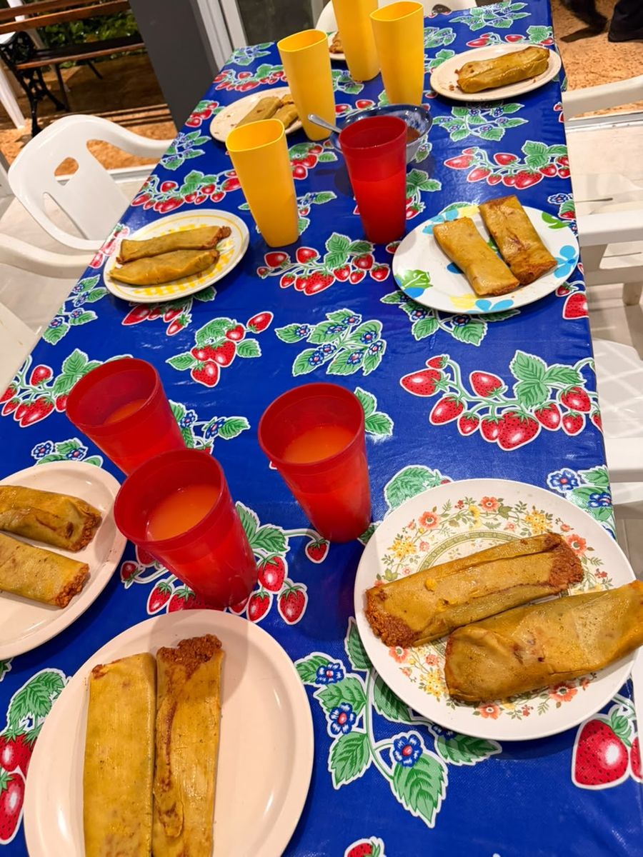 Mesa servida con tamales y vasos de agua sobre un mantel de fresas.
